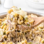 Philly Cheesesteak Pasta in a skillet and a wooden spoon lifting some of it