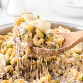 Philly Cheesesteak Pasta in a skillet and a wooden spoon lifting some of it