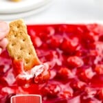 a hand dipping a biscuit into Cherry Cheesecake Dip