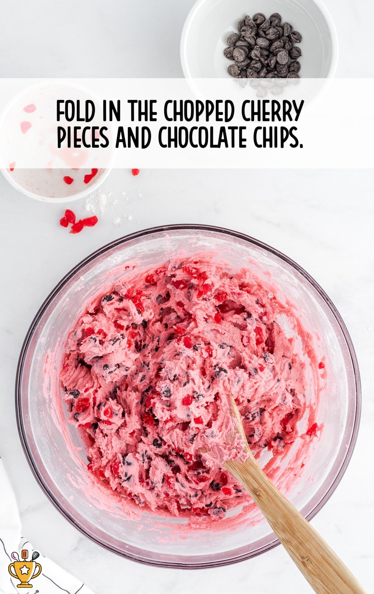 chopped cherry pieces and chocolate chips combined together in a clear bowl with a wooden spoon in it