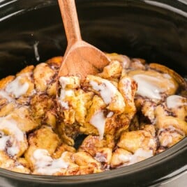 Crockpot Cinnamon Roll Casserole with a wooden cooking spoon