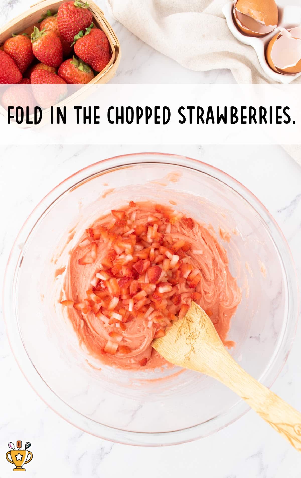 chopped strawberries mixed in a clear bowl with a wooden spoon in it