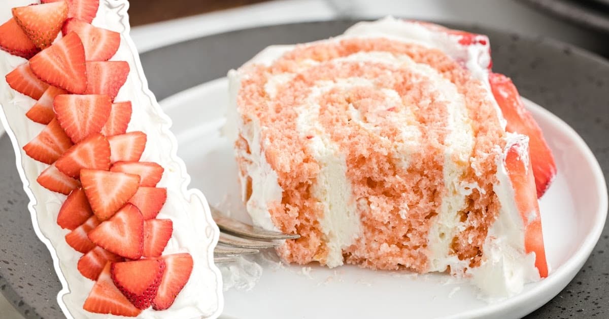 a piece of Strawberry Roll Cake on a plate with sliced strawberries on the side