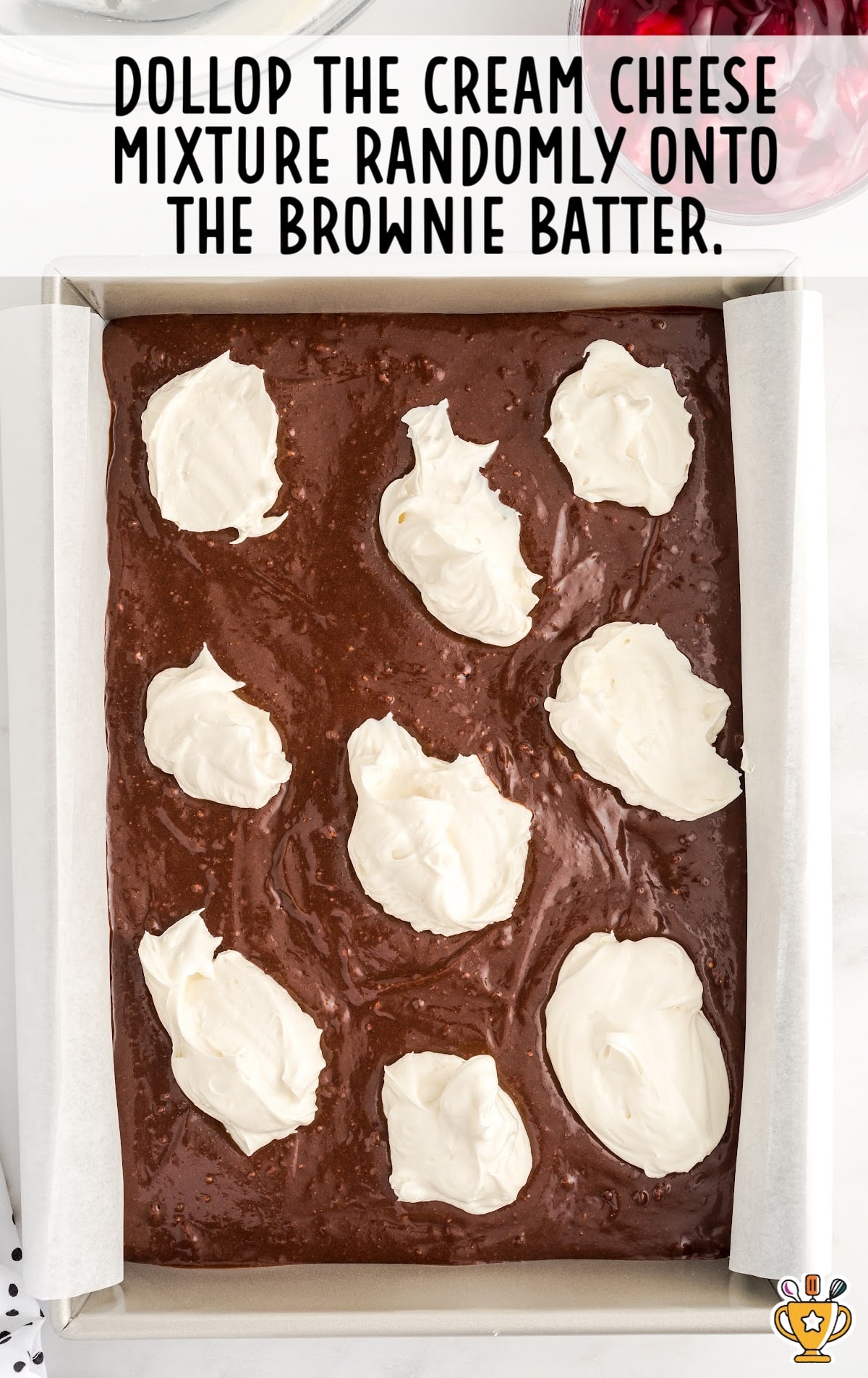 The brownie mix has dollops of cream cheese mixture on it.