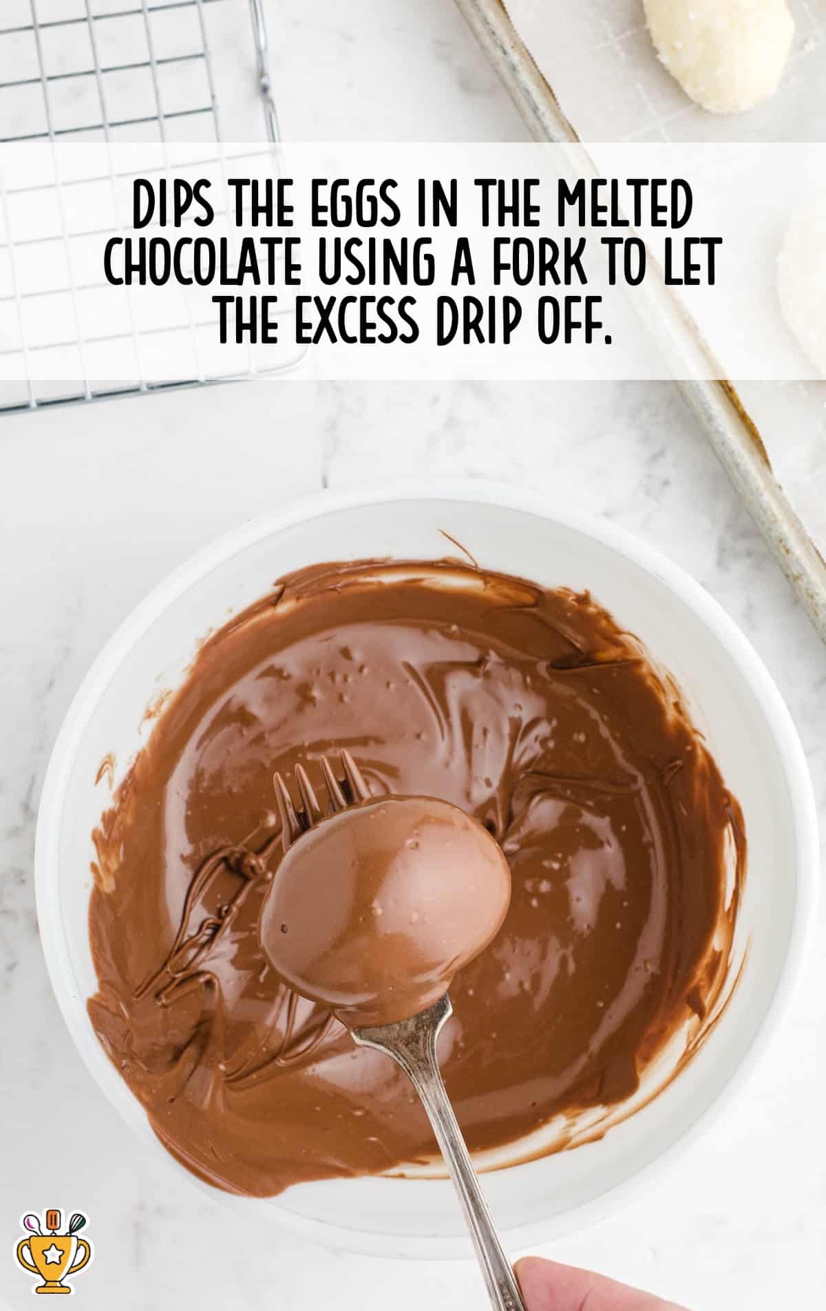 a fork holding an egg dipped in melted chocolate in a bowl