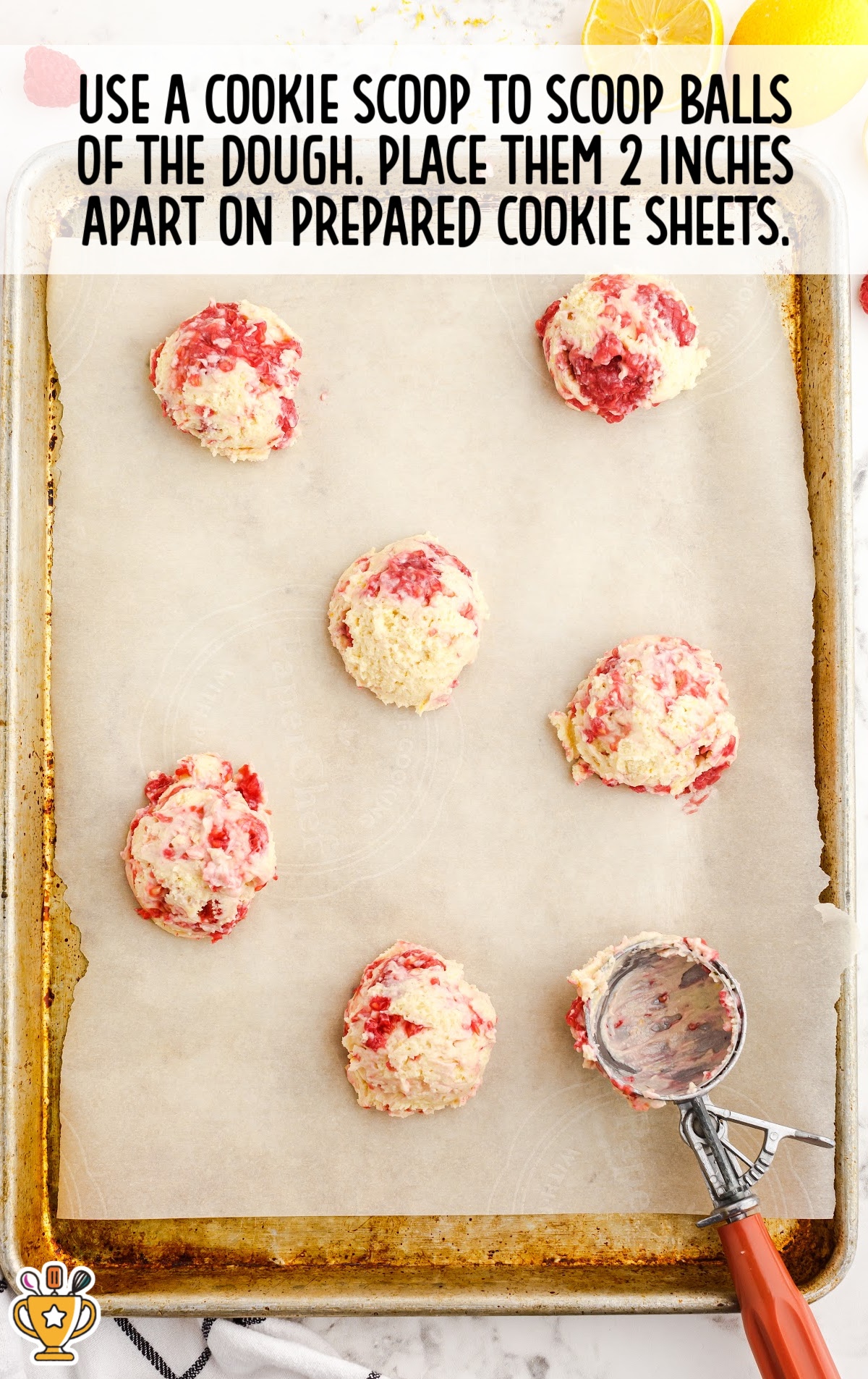 balls of the dough on a baking pan with a cookie scoop on the side
