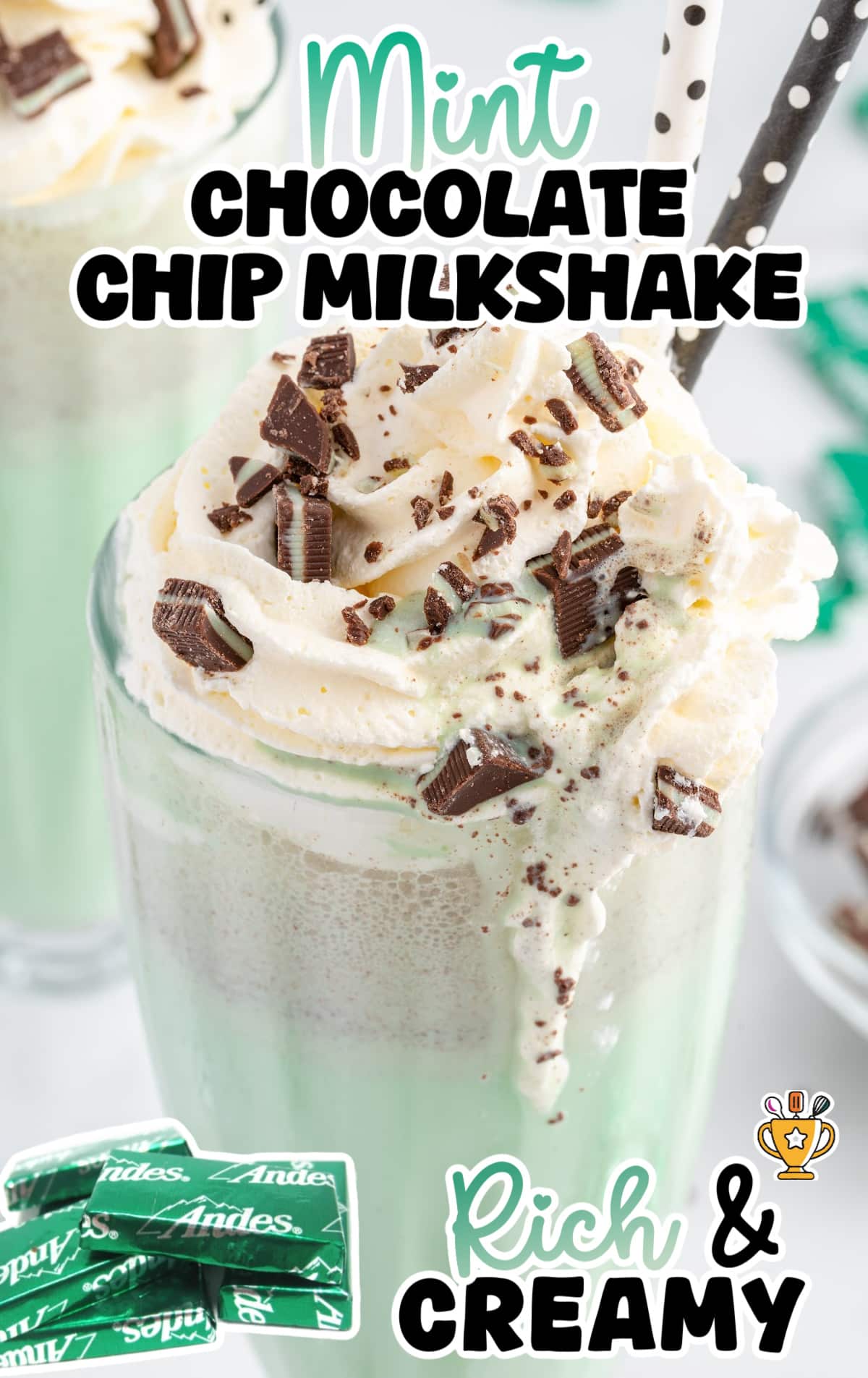A glass is filled with a mint chocolate chip milkshake, garnishes with whipped cream and andes mints.
