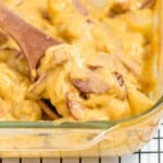 a wooden spoon holding some Kielbasa and Potato Casserole in a baking dish