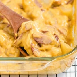 a wooden spoon holding some Kielbasa and Potato Casserole in a baking dish