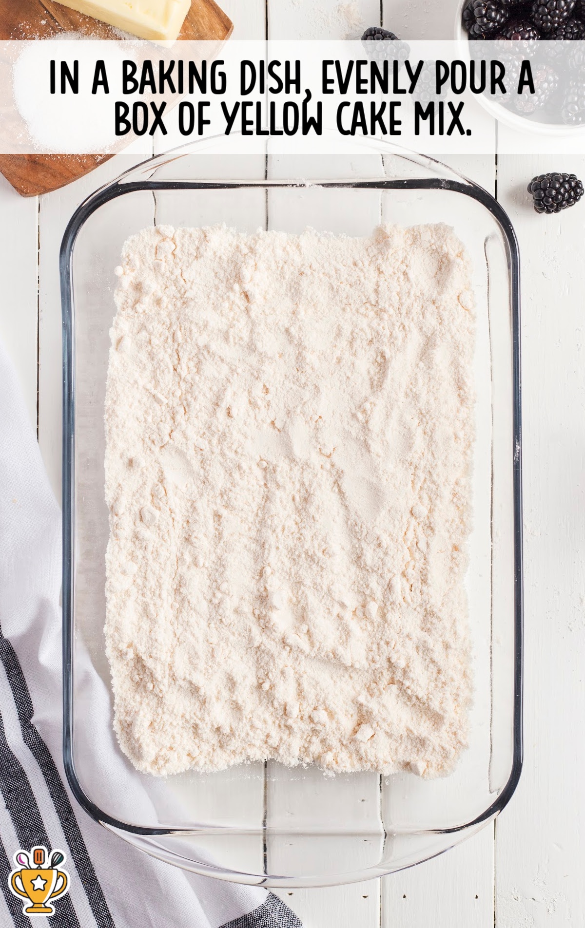 Box of yellow cake mix spread evenly in a glass baking dish on white wooden table