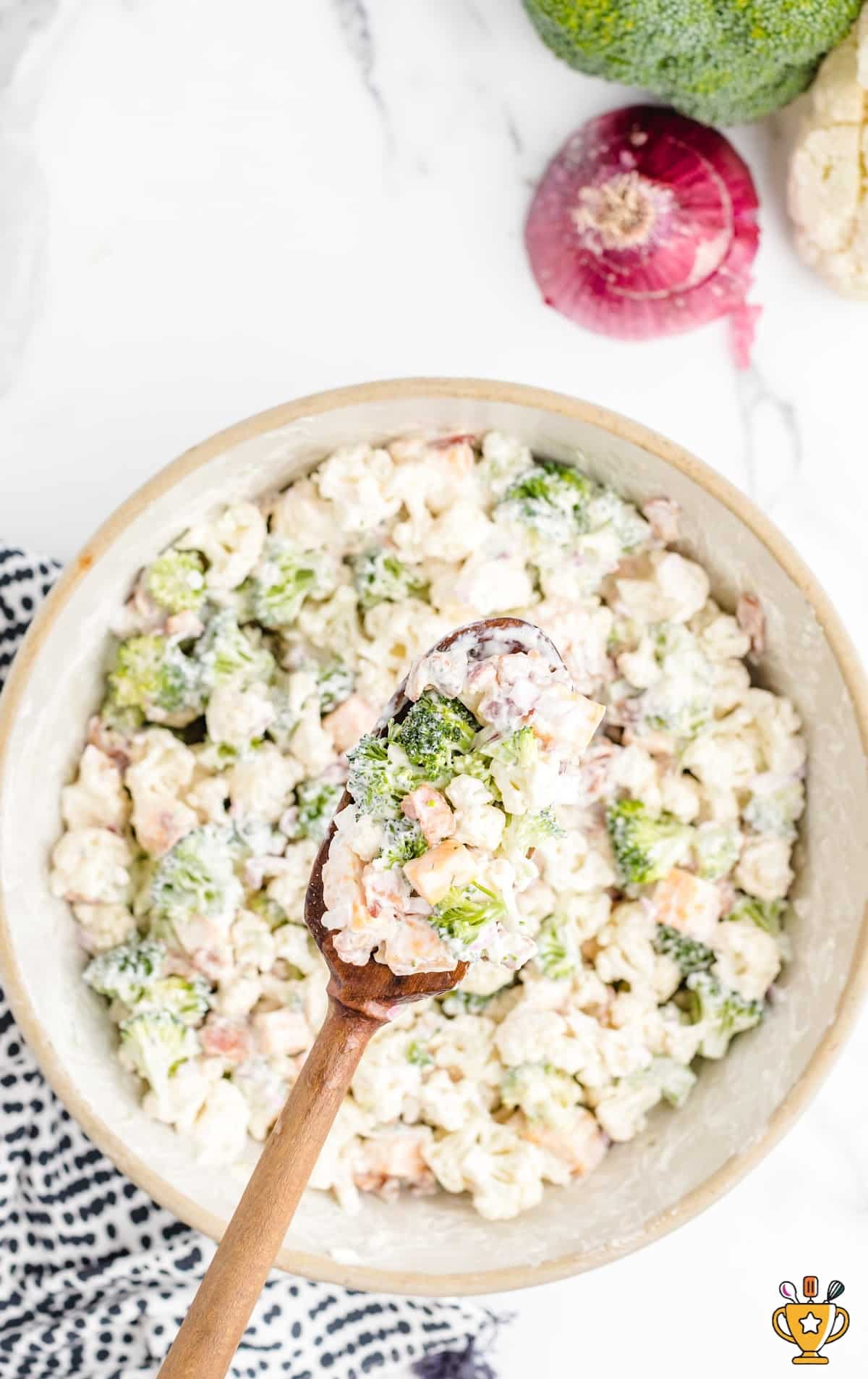 Broccoli Cauliflower Salad in a bowl with a wooden spoon holding some