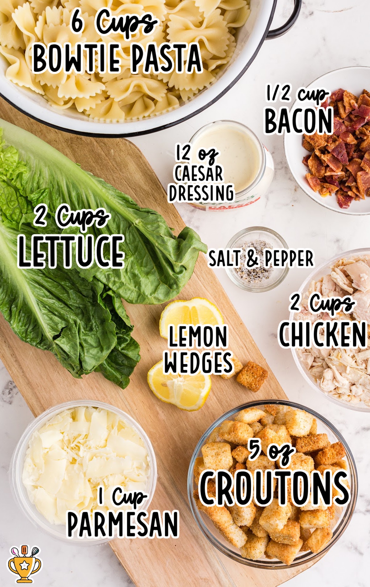 Flat lay of Caesar pasta salad ingredients including cooked bowtie pasta, lettuce, bacon, chicken, parmesan, dressing, and croutons.