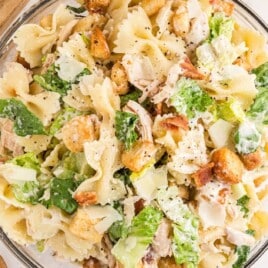 Large glass bowl filled with creamy Caesar pasta salad made with farfalle pasta, lettuce, chicken, croutons, and parmesan cheese.
