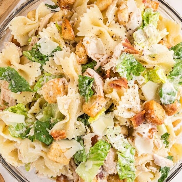 Large glass bowl filled with creamy Caesar pasta salad made with farfalle pasta, lettuce, chicken, croutons, and parmesan cheese.