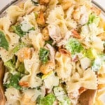 Overhead view of Caesar pasta salad in a large glass bowl with bowtie pasta, lettuce, chicken, and croutons, with text overlay reading &ldquo;So Creamy and So Fresh.&rdquo;