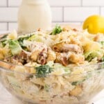 Side view of a large glass bowl filled with creamy Caesar pasta salad made with chicken, romaine lettuce, croutons, parmesan, and farfalle pasta.