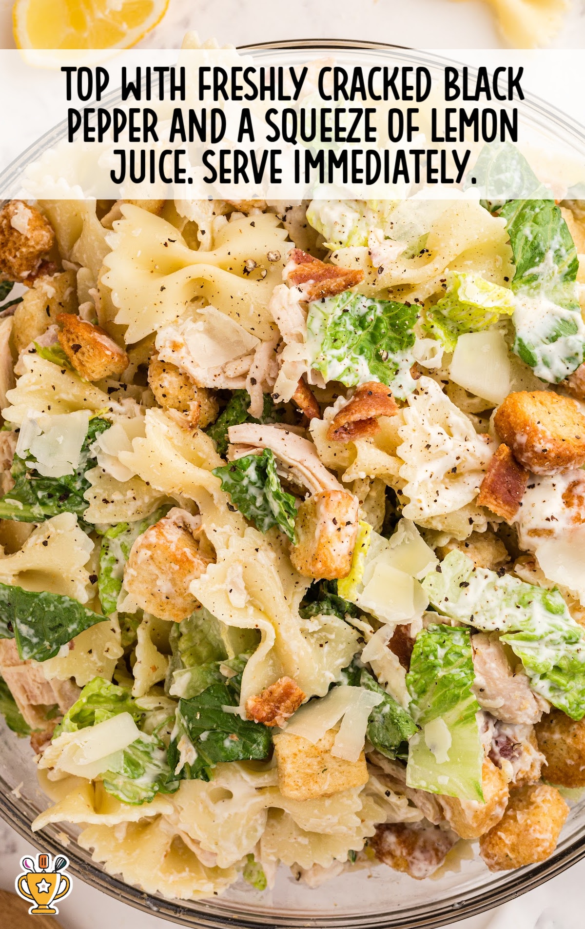 Close-up of Caesar pasta salad topped with cracked black pepper and a squeeze of lemon juice, ready to serve in a clear bowl