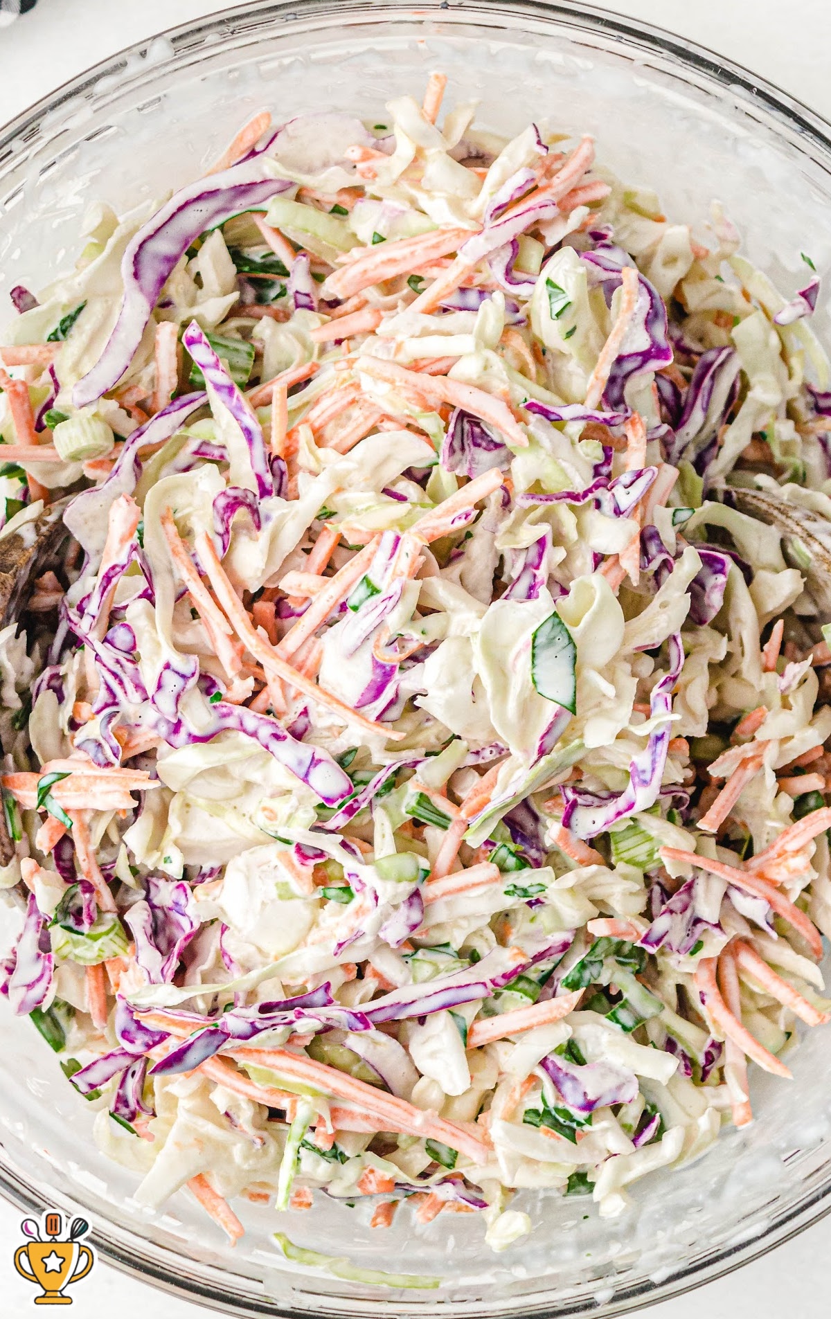 A large clear bowl filled with colorful coleslaw, with mayonnaise dressing coating shredded cabbage, carrots, and herbs.