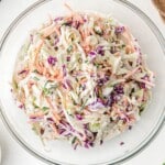 A large bowl filled with creamy classic coleslaw, featuring green onions, shredded cabbage, and carrots in a thick dressing.
