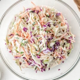 A large bowl filled with creamy classic coleslaw, featuring green onions, shredded cabbage, and carrots in a thick dressing.
