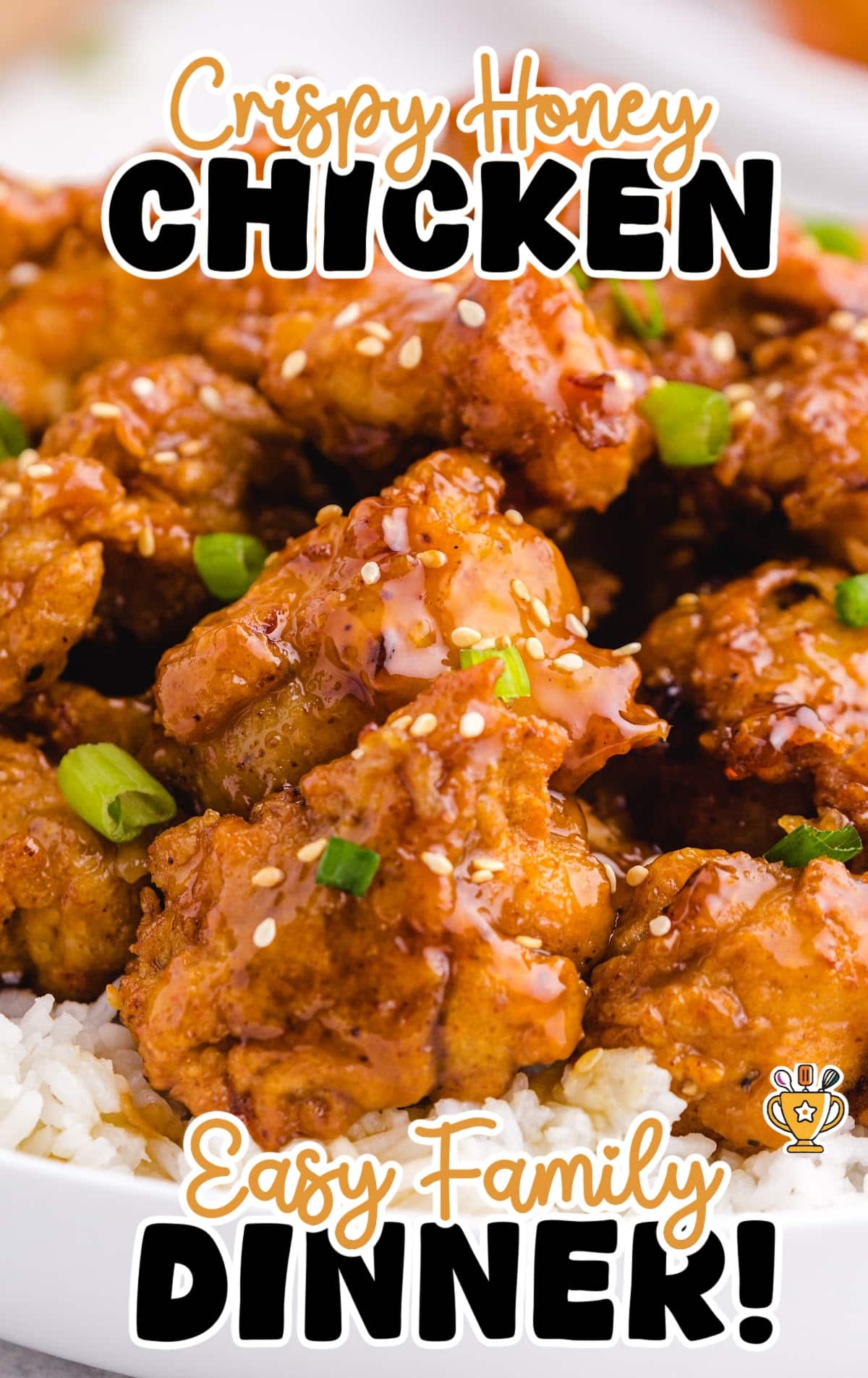 &ldquo;Glazed crispy honey chicken in a bowl over rice, topped with sesame seeds and green onions. Text overlay reads: Crispy Honey Chicken, Easy Family Dinner.&rdquo;