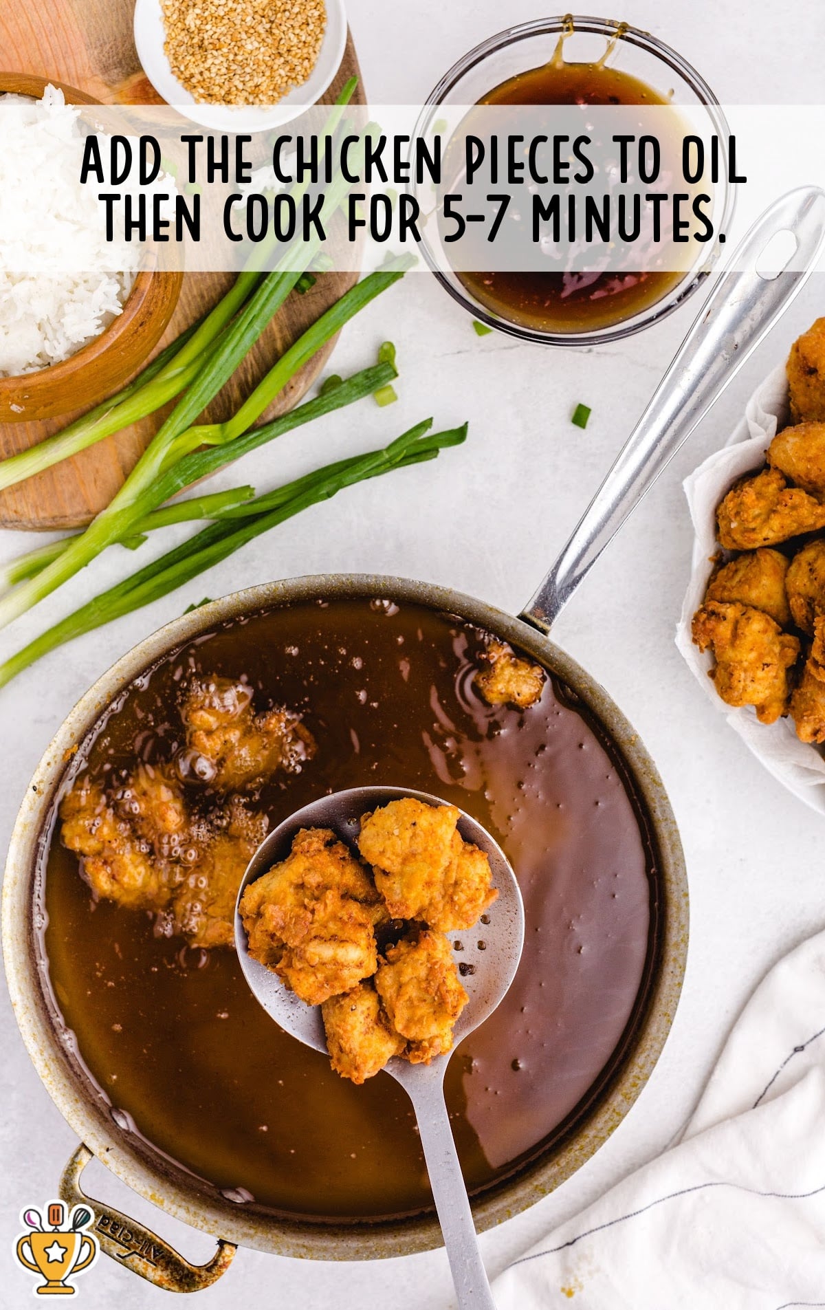 Chicken frying in a pan of oil, being scooped out with a slotted spoon.