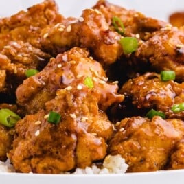 “Close-up of crispy honey chicken served over white rice, garnished with sesame seeds and chopped green onions.”