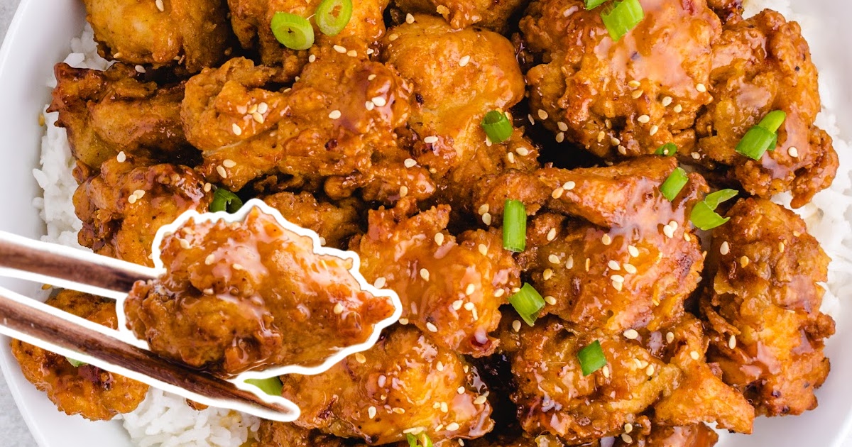 &ldquo;Overhead view of crispy honey chicken topped with sesame seeds and scallions, chopsticks holding a bite.&rdquo;