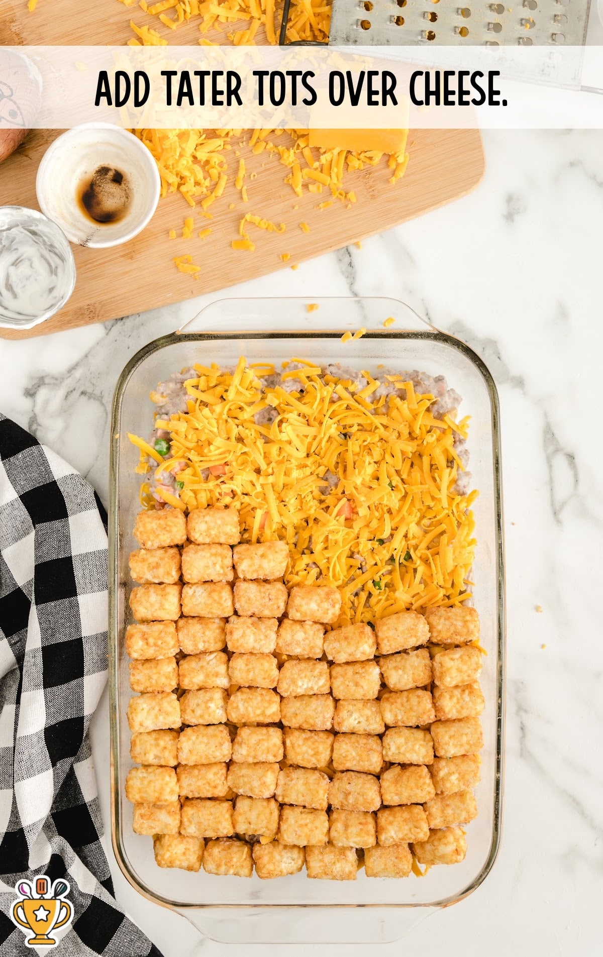Tater tots being layered on top of the shredded cheese in neat rows inside the baking dish.