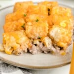 Single serving of cheesy tater tot casserole on a plate, showing creamy ground beef, corn, and melted cheddar tucked beneath crispy tots.
