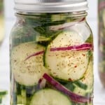 Close-up of a mason jar filled with pickled cucumber salad, featuring cucumber slices, red onion, and dill, labeled fresh and so simple.