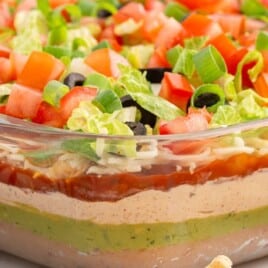 Side view of a glass dish filled with vibrant 7 layer dip, clearly showing each distinct layer and topped with fresh veggies.