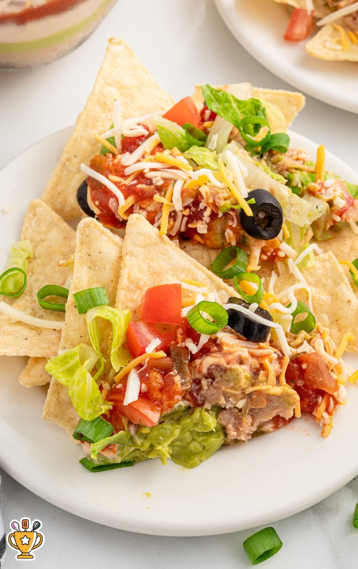 Plate of tortilla chips loaded with 7 layer dip ingredients including guacamole, beans, cheese, and fresh vegetables.