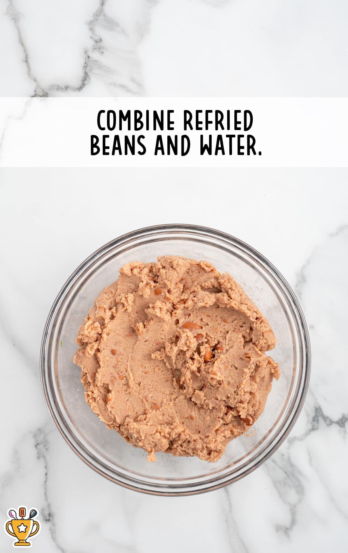 Overhead shot of a bowl filled with mashed refried beans on a white marble surface. Text overlay reads "Combine refried beans and water."