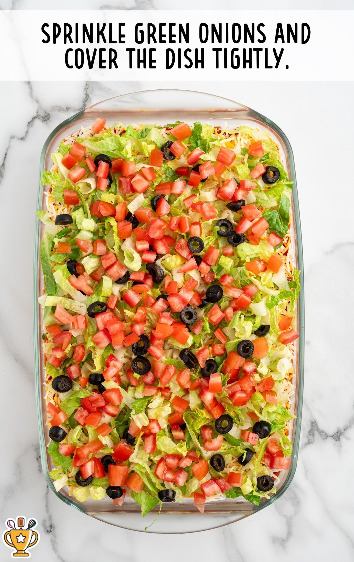 Final step showing the dish with a sprinkle of chopped green onions, completing the topping layer of the 7 layer dip before it is covered.