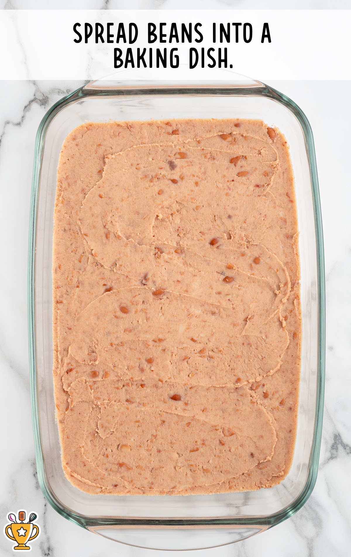 Glass baking dish filled with an even layer of refried beans, smoothed across the bottom. Text overlay says "Spread beans into a baking dish."