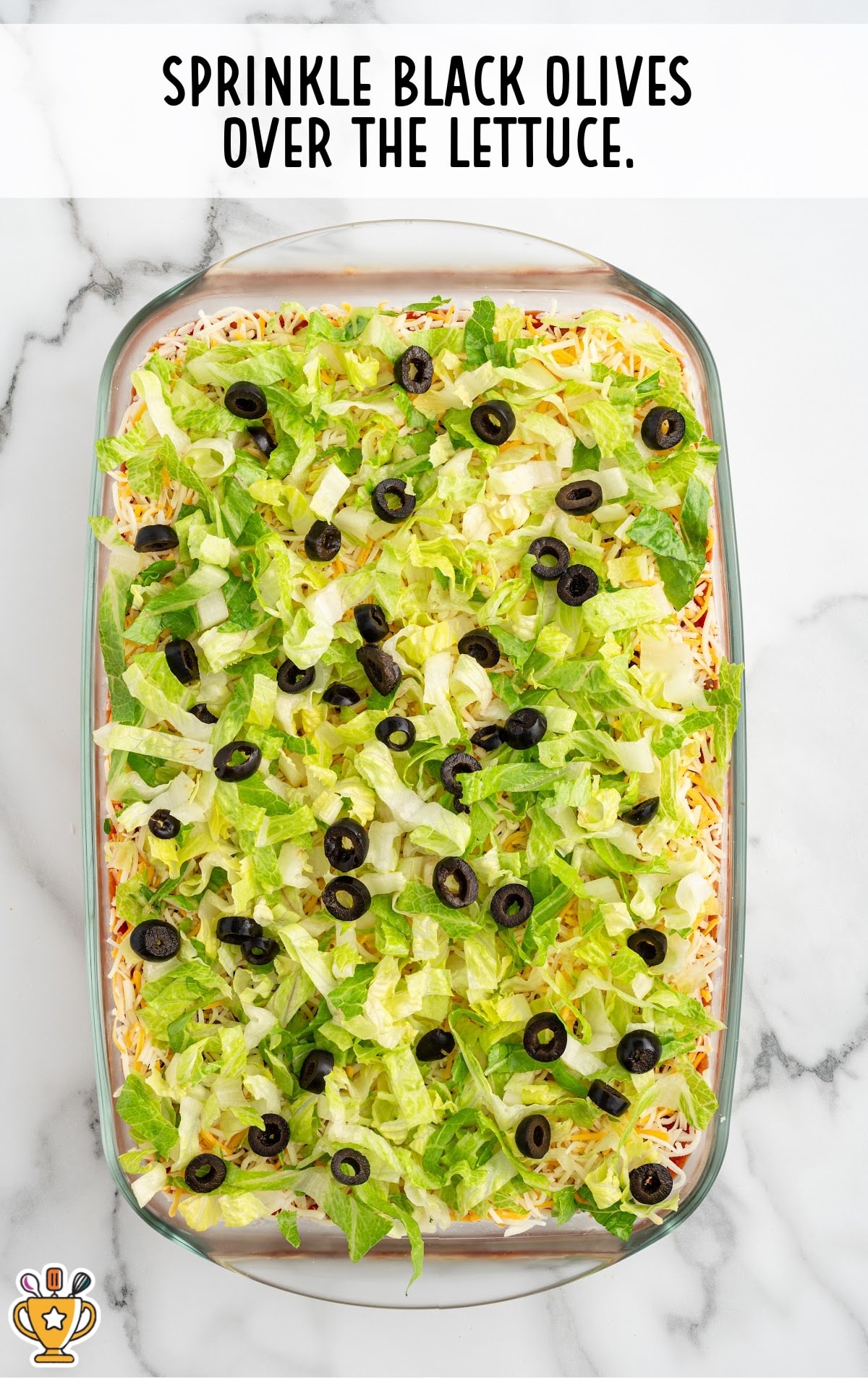 The same dish, now topped with sliced black olives scattered over the lettuce layer, adding a contrast of color and texture.