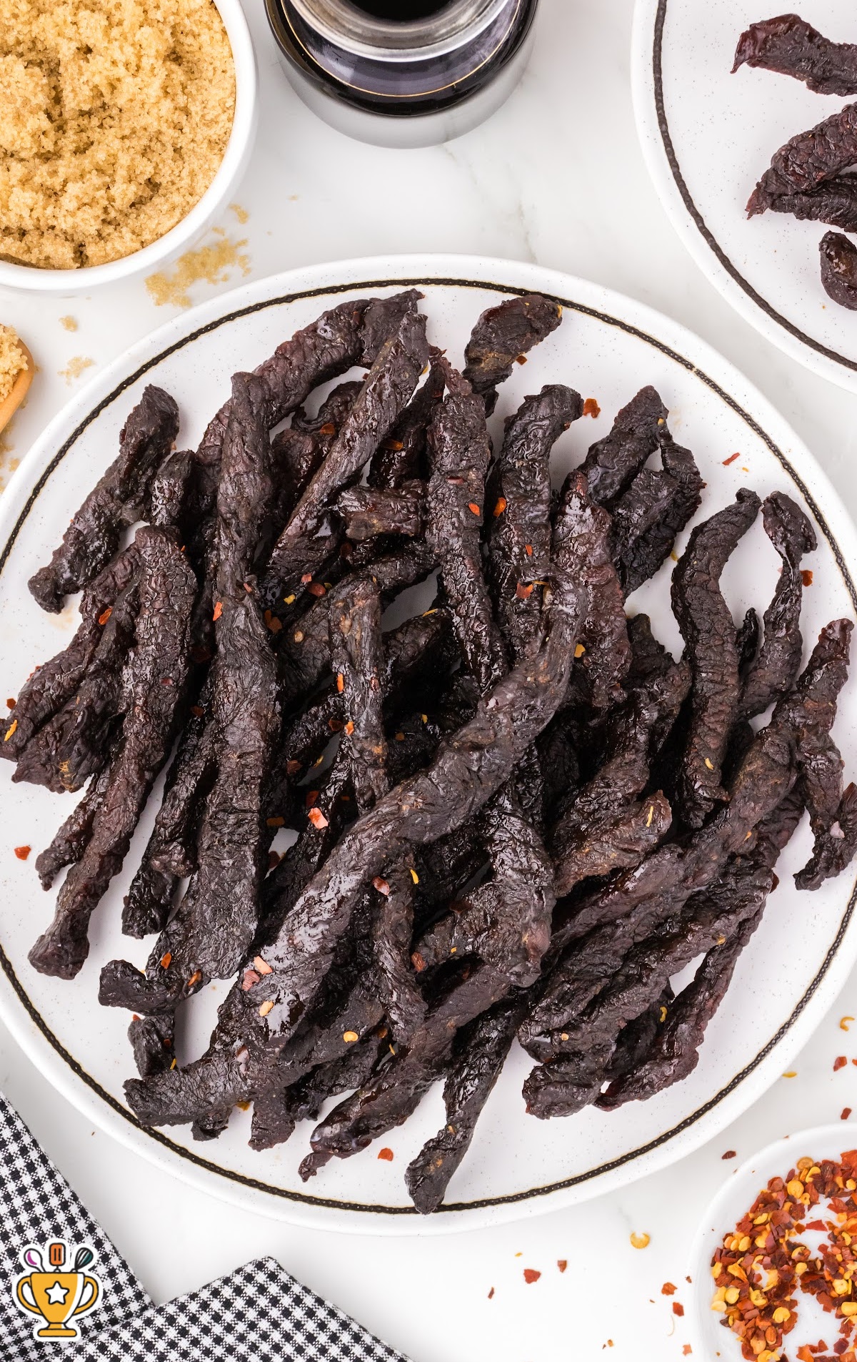 Round white plate filled with dark, glossy teriyaki beef jerky sprinkled with red pepper flakes.