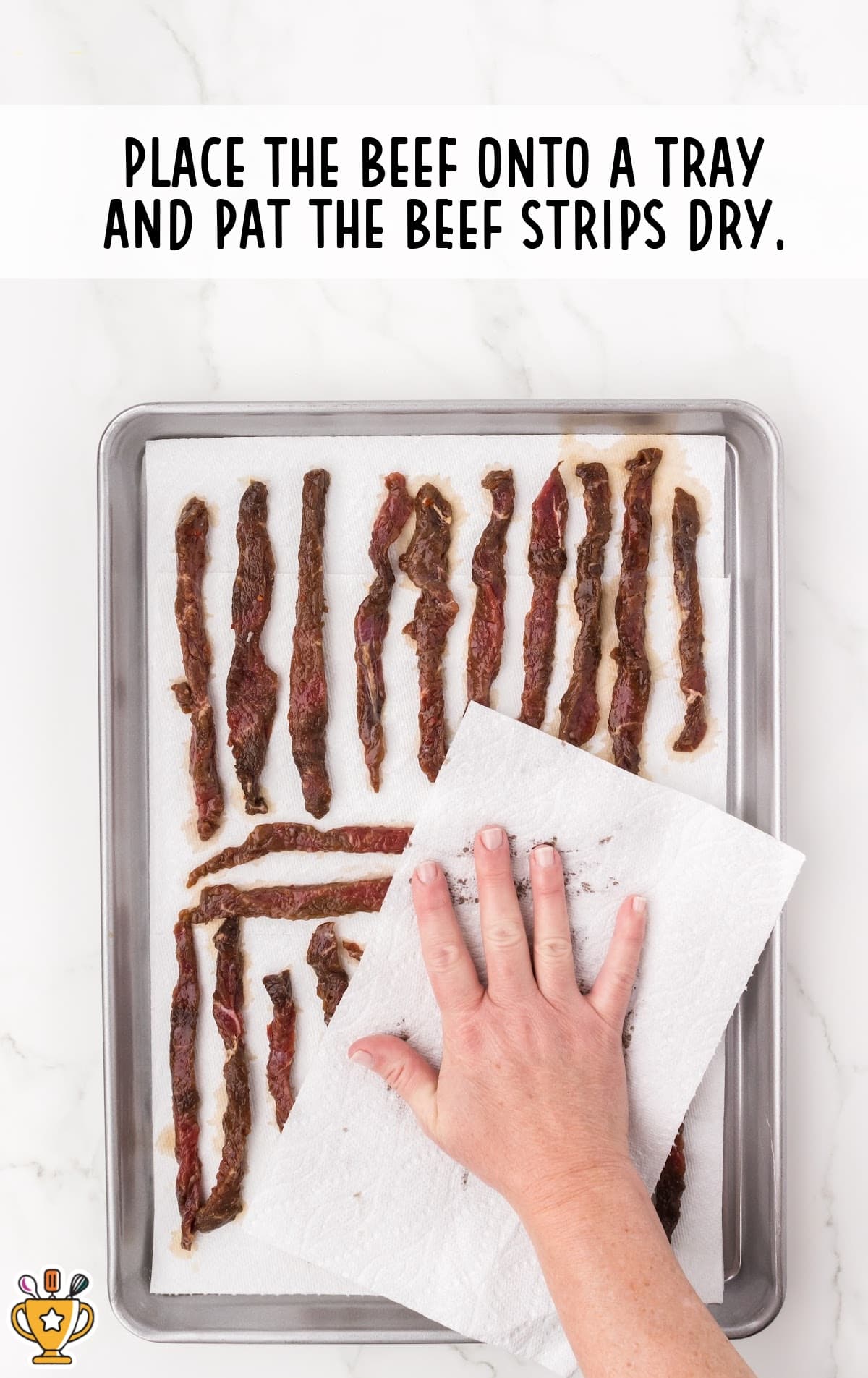 Hand patting beef strips dry with paper towels on a lined baking tray before air frying.