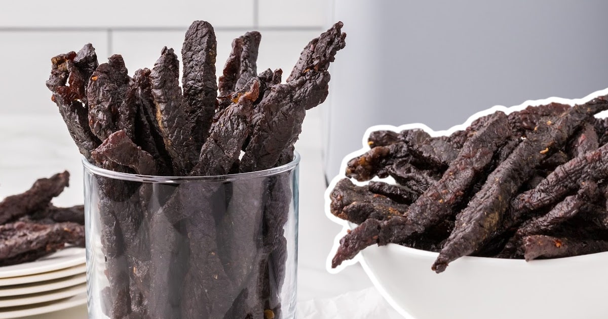 Side-by-side bowls of teriyaki beef jerky, one in a glass and the other in a white bowl, with stacked plates in background.