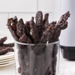 A clear glass jar is full of strips of teriyaki beef jerky.
