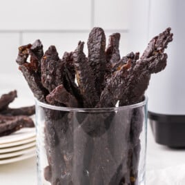 A clear glass jar is full of strips of teriyaki beef jerky.