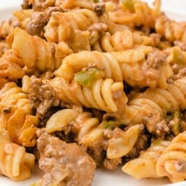 Rotini pasta mixed with ground beef and peppers, served on a white plate with creamy tomato sauce in the background.