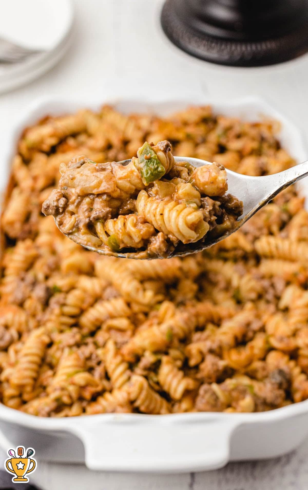 Close-up shot of a heaping spoonful of baked Amish casserole above a dish full of cheesy, beefy pasta.