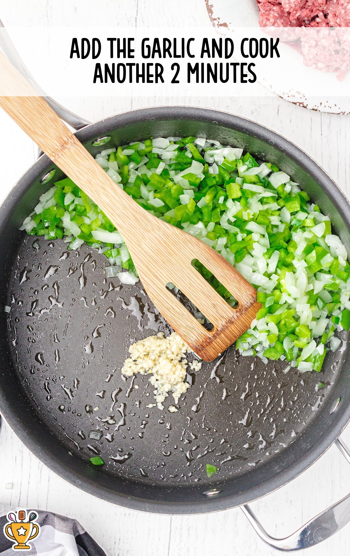 Diced garlic added to the skillet with saut&eacute;ed green bell peppers and onions, with a wooden spatula resting across the pan.