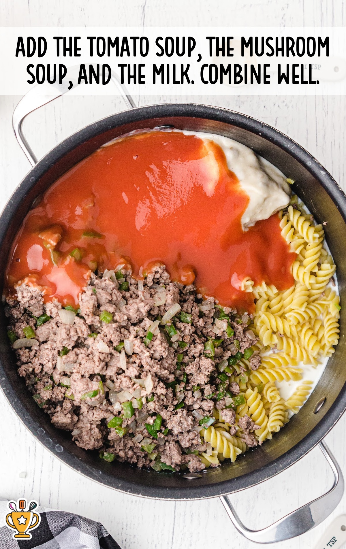 Large pot filled with cooked ground beef, saut&eacute;ed vegetables, dry rotini pasta, tomato soup, cream of mushroom soup, and milk before mixing together.