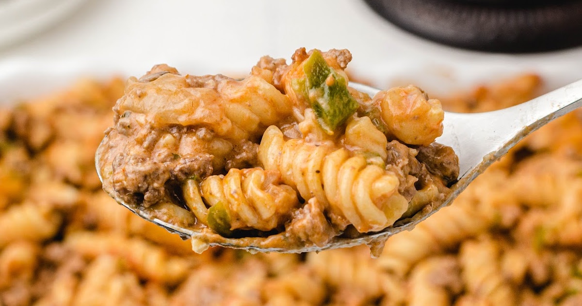 Spoonful of Amish casserole with rotini, beef, and green peppers held above a full baking dish.