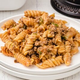 Plate of Amish casserole showing spiraled rotini pasta with tomato-based beef sauce and green peppers, styled on a white wooden background for a recipe card layout.