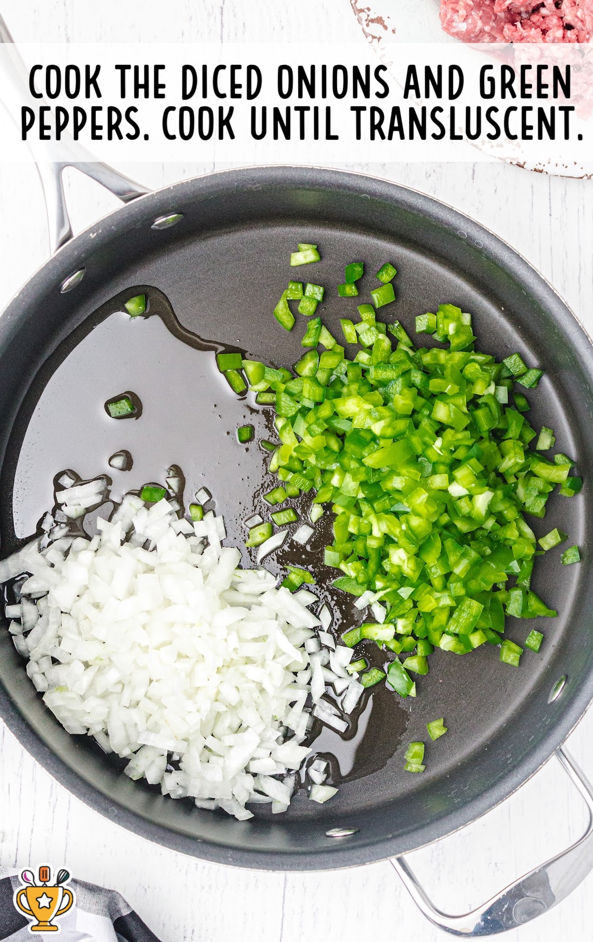 Overhead view of chopped onions and green bell peppers saut&eacute;ing in a skillet with oil as the first step of the recipe.