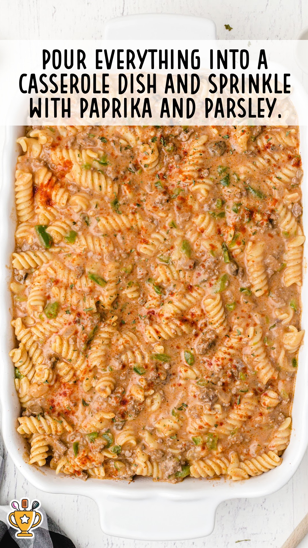 Creamy beef and pasta mixture poured into a white casserole dish, topped with paprika and parsley before baking.
